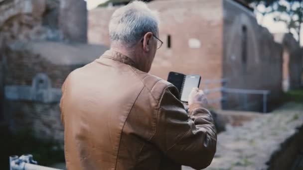 Buon uomo anziano europeo scattare foto smartphone di antiche rovine della città di Ostia, Italia in viaggio di vacanza in pensione . — Video Stock