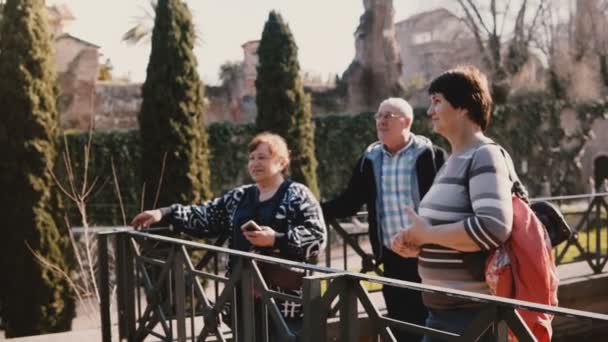 Счастливые старшие кавказские друзья, стоя вместе в красивом парке, улыбаются и разговаривают на отдыхе на Римском форуме, Италия . — стоковое видео