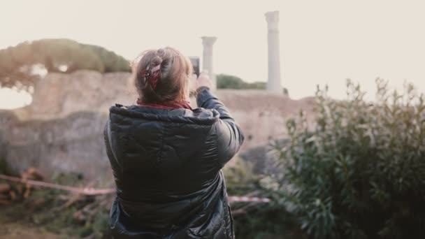 Widok z tyłu szczęśliwy senior uśmiechający się kobiety Kaukaska biorąc zdjęcie wykonane smartfonem starożytne ruiny w Ostia, Włochy na wakacjach — Wideo stockowe