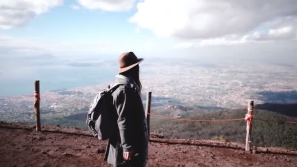 Вид сбоку на молодую красавицу-туристку с рюкзаком, спускающуюся с вулкана Увий, наслаждающуюся видом на город . — стоковое видео