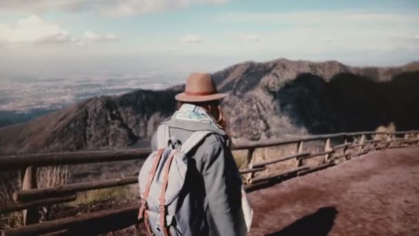 Обратный вид молодой веселой туристической девушки с камерой, спускающейся с вулкана Везувий, поворачивающейся и улыбающейся . — стоковое видео