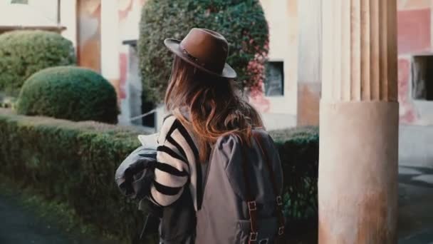 Achteraanzicht van Kaukasische toeristische meisje met rugzak verkennen van oude tuin met pilaren en fresco's in Pompeii, Italië. — Stockvideo