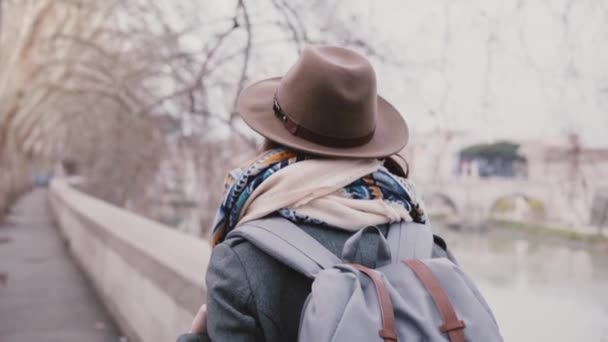 Задний вид вдумчивой туристки с рюкзаком прогулка вдоль реки Тибр под платанами зимой Рим замедленного движения — стоковое видео