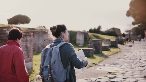 Cámara sigue madre e hija caucásica con un mapa que explora antiguas ruinas históricas de Ostia, Italia cámara lenta . — Vídeos de Stock