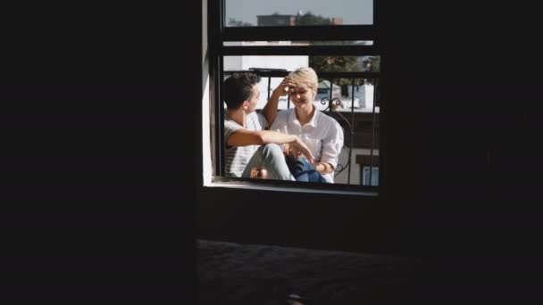 Aparat zbliżających się piękna Młoda para romantyczny siedzący blisko siebie, przytulanie i mówienie o mały słoneczny balkon. — Wideo stockowe