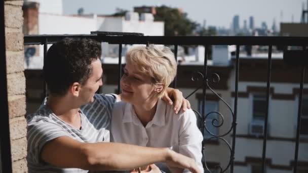 Jeune femme européenne et homme hispanique prenant un café au petit balcon ensoleillé avec des tasses métalliques en bronze, parler et sourire . — Video