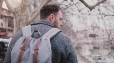 Yakın çekim yavaş hareket emin beyaz işadamı tatile Tiber Nehri banka yürüyüş sırt çantası ile vurdu.
