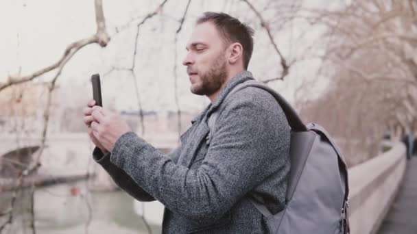 Молодой успешный бизнесмен-турист фотографируется на смартфоне на берегу реки Тибр в Риме, Италия на отдыхе осенью . — стоковое видео