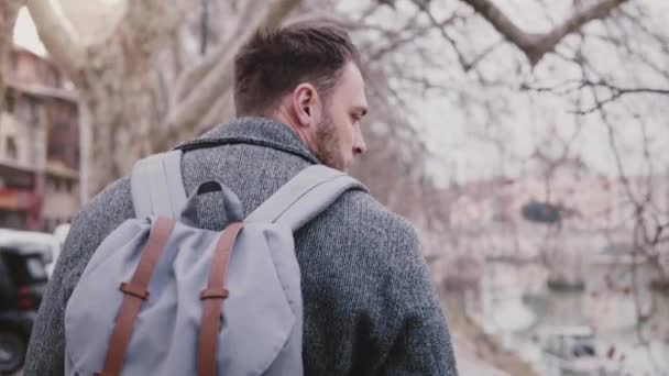 Close-up slow motion shot of confident Caucasian businessman with backpack walking along Tiber river bank on vacation. — Stock Video