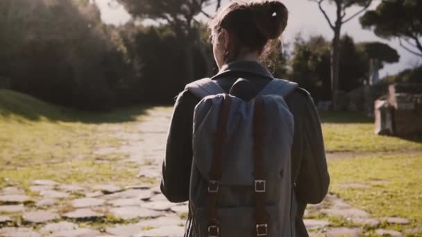 Rückseite attraktive Reise-Bloggerin Mädchen mit Rucksack und Karte erkundet alte sonnige Ruinen in Ostia Zeitlupe. — Stockvideo