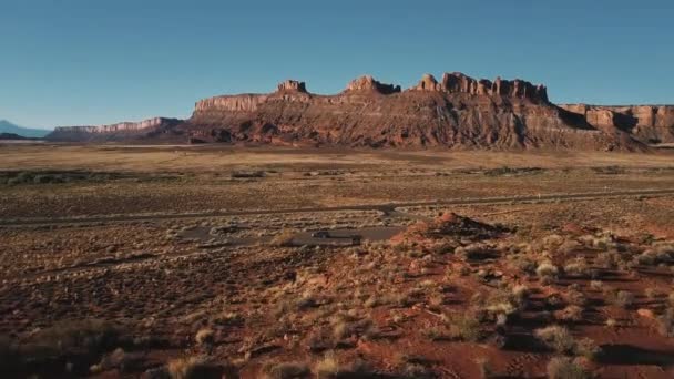 Drone flying low above dry desert landscape with flat mountains, approaching silver minivan car near small highway road. — Stock Video