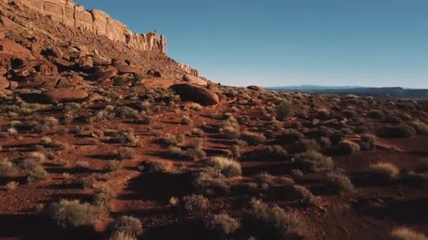 Беспилотник летит низко над землей возле массивной горы, пейзаж песчаника покрыт скалами и солнечным небом в Аризоне . — стоковое видео