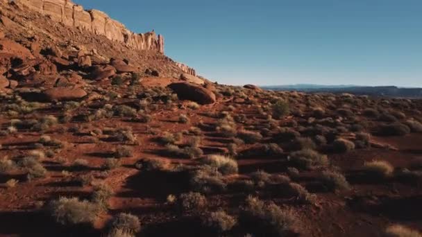 Drona zburând jos deasupra solului în apropierea unui munte masiv, peisaj din gresie acoperit cu pietre și cer însorit în Arizona . — Videoclip de stoc