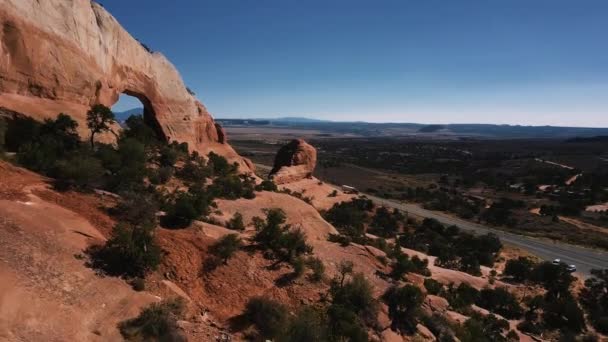 Drone flying poblíž velké skalní útvar s velkou dírou pokryté keříky, turisté kochat výhledem na horské pouště. — Stock video