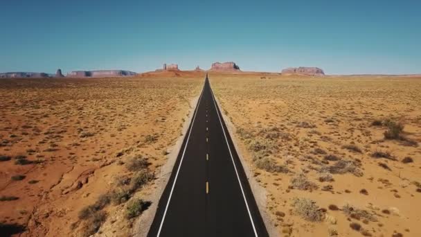 Drone flying backwards over iconic empty sandstone desert road in Monuments Valley, Arizona with big cliff mountains. — Stock Video