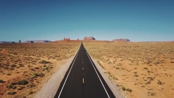 Drone follows car moving along iconic American desert highway road in Monuments Valley with big cliff mountains skyline. — Stock Video