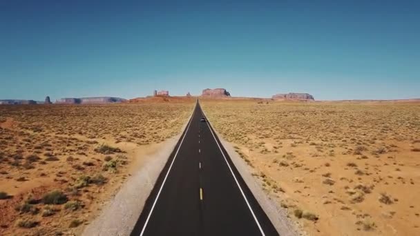 Drohne verfolgt Auto, das sich entlang der ikonischen amerikanischen Wüsten-Highway-Straße im monumentalen Tal mit großer Skyline der Klippen bewegt. — Stockvideo