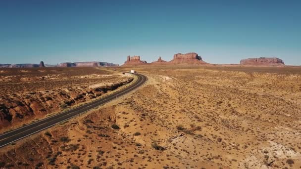 記念碑の谷、米国で素晴らしい山スカイラインと砂漠高速道路道路に沿って移動する赤い貨物トラックの空中ショット. — ストック動画