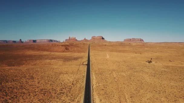 Drone flying backwards high above empty sandstone desert road in Monuments Valley, Arizona with flat mountains skyline. — Stock Video