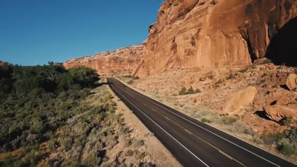 Drone follows silver car driving on highway between big steep canyon rocky mountain, bushy desert greenery and trees. — Stock Video