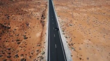 Dronu takip ve gümüş renkli araba güneşli Amerikan çöl manzara sevk üstünde boş Otoban yol üzerinde yakınlaştırma.