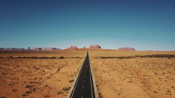 Drone segue carro de prata dirigindo ao longo da famosa estrada do deserto americano ensolarado em monumentos vale em arizona e utah — Vídeo de Stock