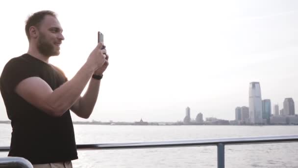 Feliz sonriente viajero europeo haciendo una videollamada usando un smartphone en un viaje en barco por Nueva York en cámara lenta . — Vídeos de Stock