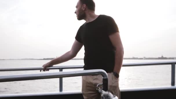 Feliz joven relajado sonriente hombre de pie junto a una cerca del barco disfrutando de la vista, alejándose de la cámara en cámara lenta . — Vídeos de Stock