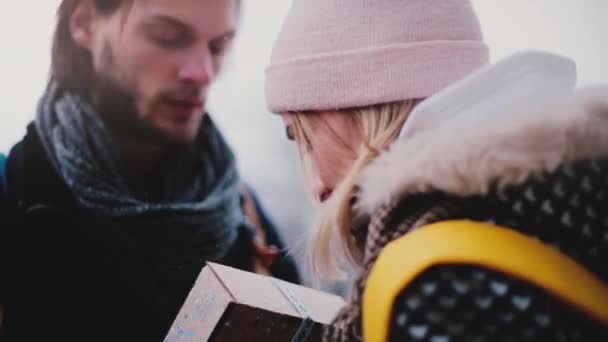 Nahaufnahme eines glücklichen, gut aussehenden jungen Mannes, der seiner Freundin an einem verschneiten Neujahrstag eine Geschenkbox schenkt. — Stockvideo