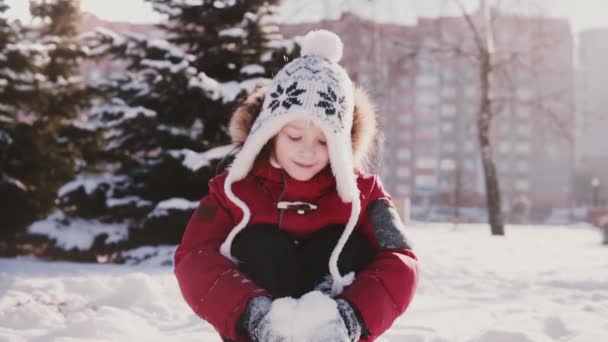 Cute little happy European girl in winter clothes looking at camera, throwing snow in the air and smiling slow motion. — Stock Video