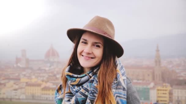 Close-up portrait of young beautiful Caucasian girl in hat smiling happy, looking at camera in Florence on a foggy day. — Stock Video