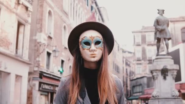 Portret van een vrouw met lang haar en hoed, het dragen van een carnaval masker permanent in Venetië straat in Italië camera kijken. — Stockvideo