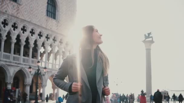 Muda bahagia Kaukasia gadis wisatawan dengan ransel tersenyum, melihat sekitar bersemangat di tua Saint Mark persegi di Venesia . — Stok Video