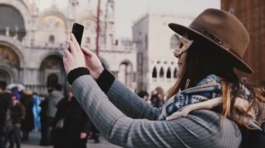 Bir şık şapka ve beyaz karnaval yüz maskesi giyen mutlu kadın Venedik şehir meydanında, İtalya gülümseyen selfie fotoğrafı çeker. Neşeli heyecan kadın gezgin heyecanlı, harika tatil seyahat zevk.