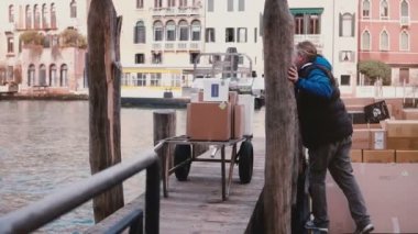 Venedik 5 Şubat 2018 sonrası kargo gondol İtalya kış sokak kanalında iskelede el arabasından yığın kutulara adam.