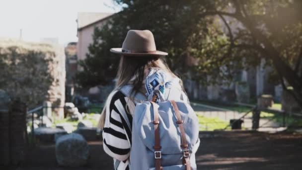 Камера следит за счастливой случайной европейской девушкой с рюкзаком прогуливаясь среди красивых руин Форума в Риме, повернув налево — стоковое видео