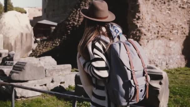 Aantrekkelijke jonge vrouwelijke toeristische met rugzak in stijlvolle hoed verkennen van het Forum in Rome rondkijken glimlachend opgewonden. — Stockvideo