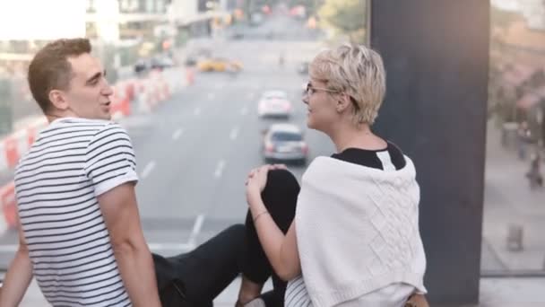 Mooie jonge multi-etnisch romantisch paar zittend op een brug, chatten, knikken en lachen over New York street. — Stockvideo
