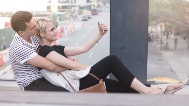 Feliz pareja romántica multiétnica sentada en un puente callejero de Nueva York, tomando selfie de teléfonos inteligentes y divirtiéndose sonriendo . — Vídeos de Stock