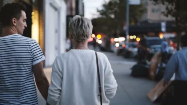 Gelukkig jong romantische koppel handen te houden wandelen langs avond Soho, New York, straatverlichting op de achtergrond wazig. — Stockvideo