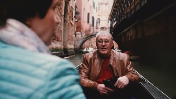 Glücklich lächelnde ältere europäische männliche Touristen hören älteren Frauen in der Gondel während der venezianischen Kanaltour zu. — Stockvideo