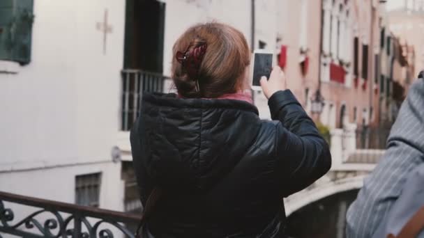 Volver ver feliz viajero senior femenino tomando foto del teléfono inteligente de la hermosa calle del canal de agua de otoño en Venecia Italia . — Vídeo de stock