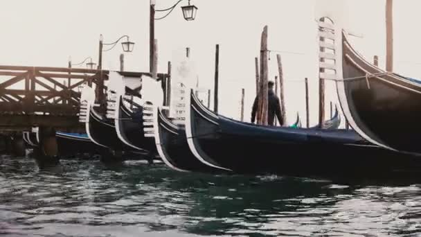 Foto media de hermosas góndolas vacías tradicionales balanceándose sobre las olas en el muelle de la laguna de madera de la mañana en Venecia, Italia . — Vídeo de stock