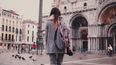 Arkadan görünüm moda kadın turist ile sırt çantası ve San Marco Venedik ağır çekimde bina Cathedral yakınındaki fotoğraf makinesi.