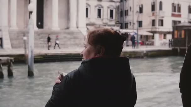 Back view excited active older Caucasian tourist woman taking smartphone photos on a gondola excursion on Venice trip. — Stock Video