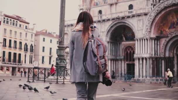 Back view fashionable woman tourist with backpack and camera near San Marco Cathedral building in Venice slow motion. — Stock Video