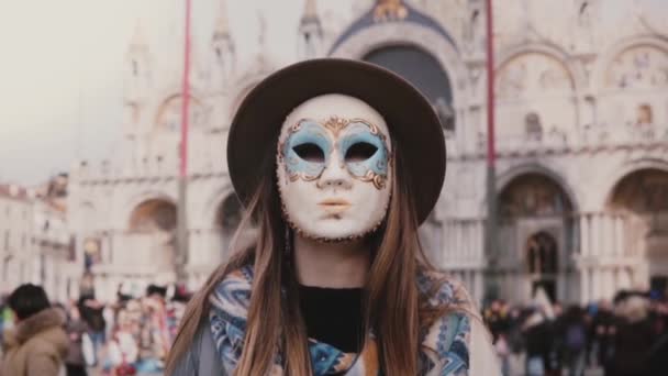 Porträt einer Frau mit langen Haaren mit Hut und Karnevalsmaske, die an der Kathedrale San Marco in Venedig in Zeitlupe steht.