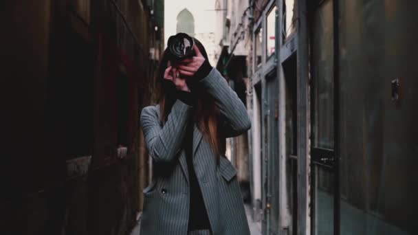 Wanita jurnalis profesional yang menarik hati berjalan dengan kamera di jalan Venesia kuno, mengambil foto gerakan lambat . — Stok Video