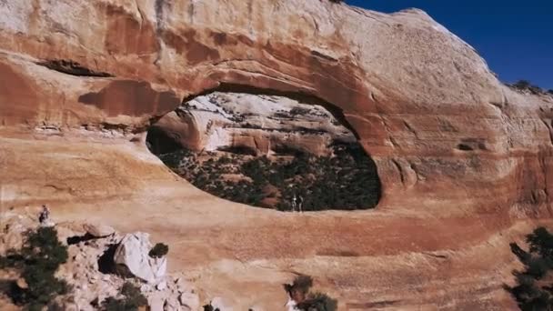 Drone flying through massive Arches rock formation with two tourists in the middle at national park reserve mountains. — Stock Video