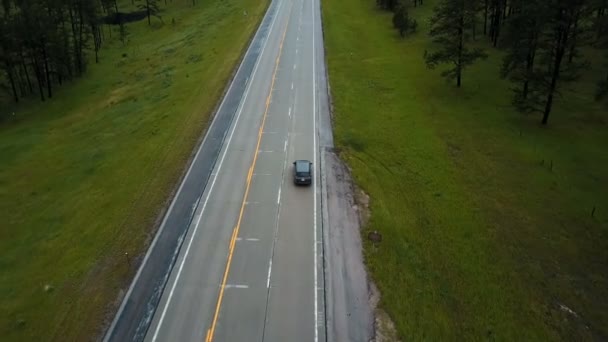 Drone follows minivan car moving along concrete highway in the middle of wild green forest hills covered with trees. — Stock Video